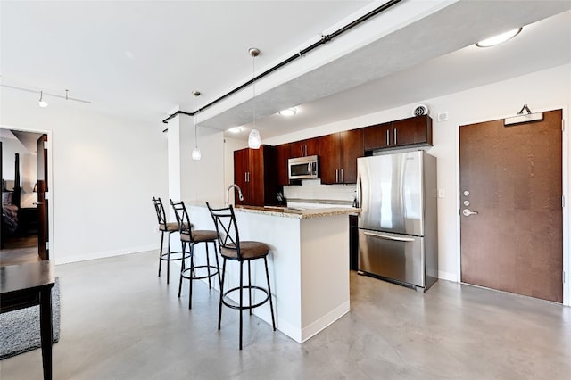 kitchen with stainless steel appliances, a kitchen breakfast bar, light stone counters, an island with sink, and decorative light fixtures