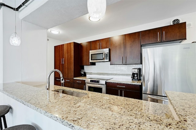 kitchen with a breakfast bar, sink, tasteful backsplash, decorative light fixtures, and appliances with stainless steel finishes