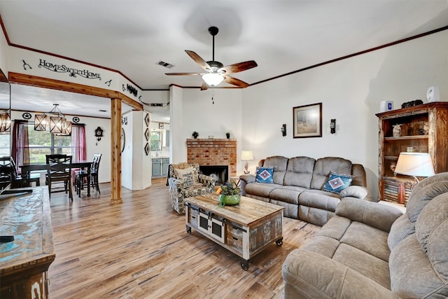 living room featuring ceiling fan with notable chandelier, light wood-type flooring, a brick fireplace, and crown molding