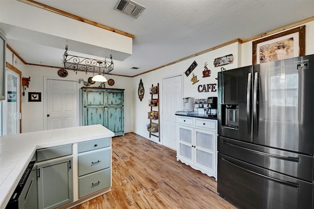 kitchen with tile countertops, light wood-type flooring, a textured ceiling, and appliances with stainless steel finishes