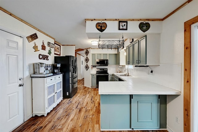 kitchen with kitchen peninsula, decorative backsplash, sink, black appliances, and wood-type flooring