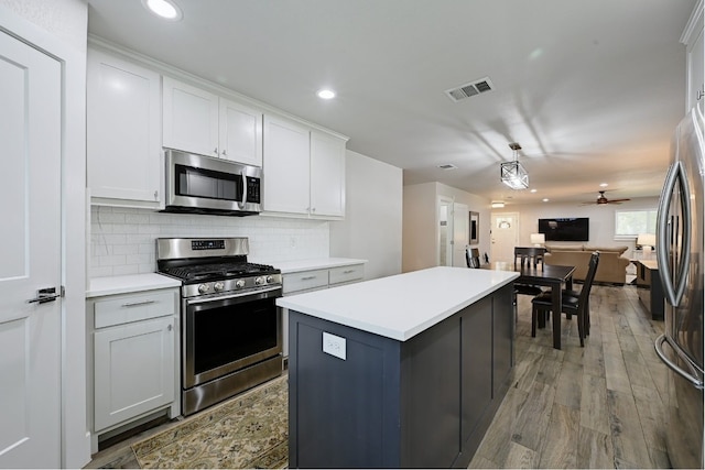 kitchen with white cabinets, hardwood / wood-style flooring, ceiling fan, appliances with stainless steel finishes, and a kitchen island