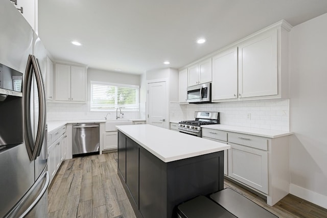 kitchen featuring light wood-type flooring, stainless steel appliances, a kitchen island, sink, and white cabinetry