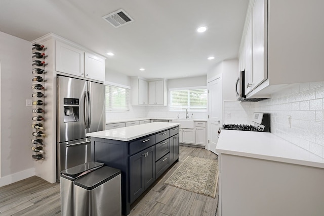 kitchen with a kitchen island, white cabinets, light wood-type flooring, and appliances with stainless steel finishes