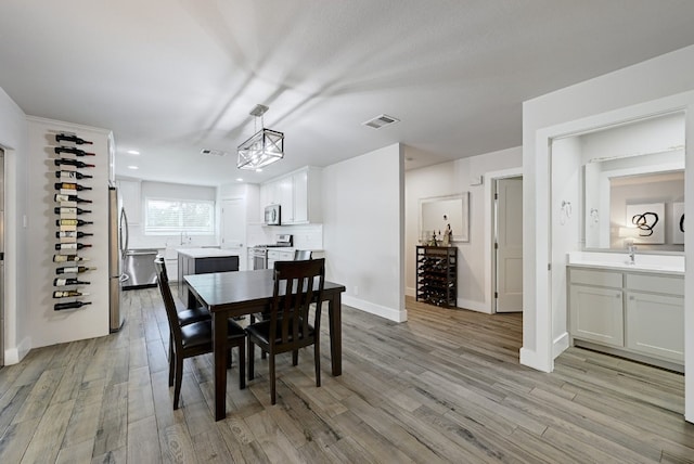 dining area with a notable chandelier, light hardwood / wood-style floors, sink, and wine cooler