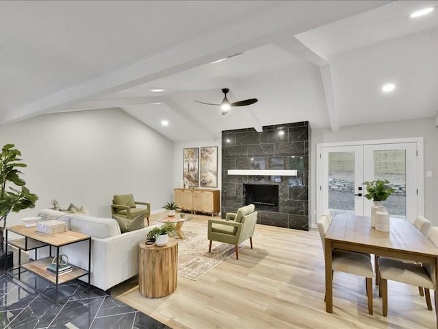 living room featuring french doors, ceiling fan, hardwood / wood-style floors, vaulted ceiling with beams, and a tiled fireplace