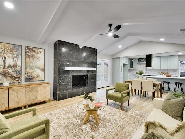 living room with vaulted ceiling with beams, light hardwood / wood-style floors, ceiling fan, and a tiled fireplace