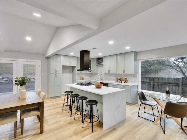 kitchen with stainless steel gas stovetop, vaulted ceiling, wall chimney exhaust hood, light wood-type flooring, and a kitchen island