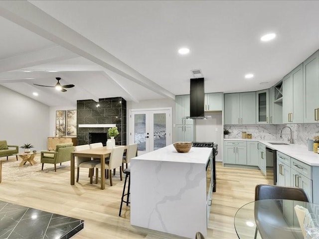 kitchen with ceiling fan, wall chimney range hood, sink, light hardwood / wood-style flooring, and a center island