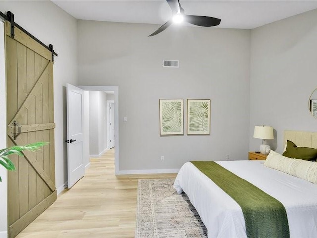 bedroom featuring ceiling fan, a barn door, light wood-type flooring, and a high ceiling