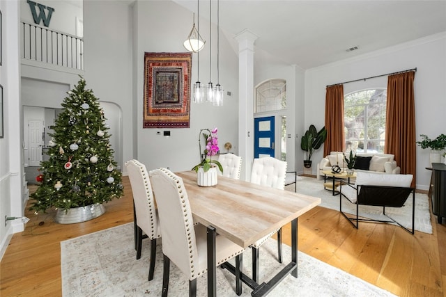 dining space with light hardwood / wood-style floors, ornate columns, and ornamental molding