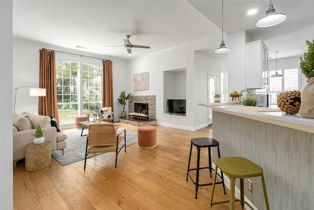 living room with ceiling fan, ornamental molding, a fireplace, and light hardwood / wood-style flooring