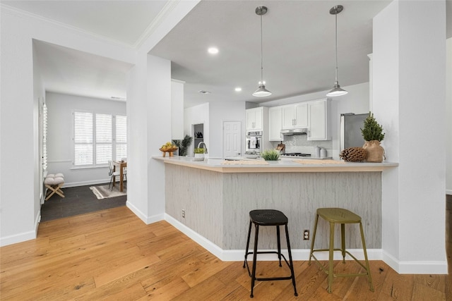 kitchen with white cabinetry, a kitchen bar, kitchen peninsula, and light hardwood / wood-style flooring