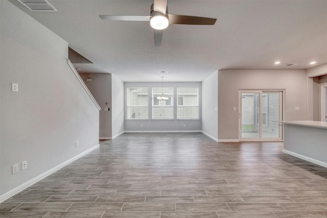 unfurnished living room featuring ceiling fan with notable chandelier and a healthy amount of sunlight