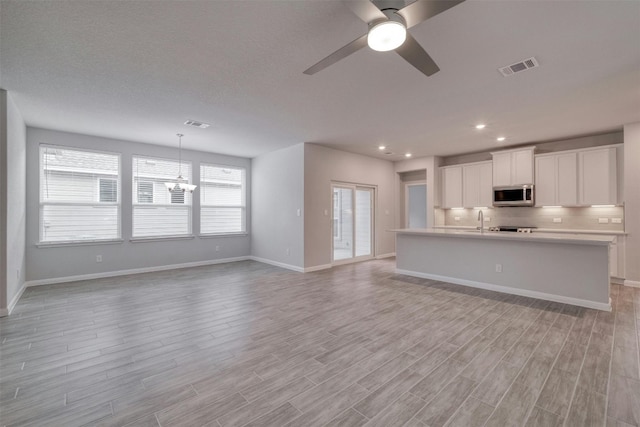 unfurnished living room featuring ceiling fan with notable chandelier and sink