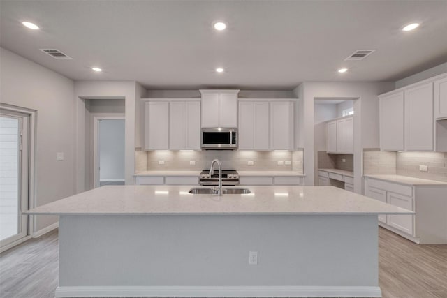 kitchen with white cabinetry, stainless steel appliances, light hardwood / wood-style floors, and an island with sink