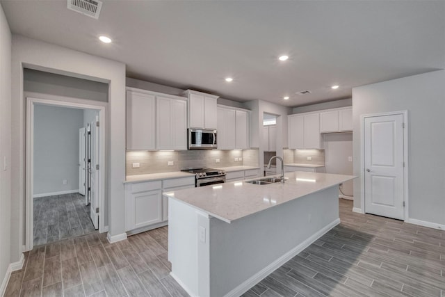 kitchen with appliances with stainless steel finishes, sink, a center island with sink, and white cabinets