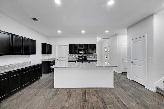 kitchen featuring a kitchen island with sink, light stone counters, decorative backsplash, dark hardwood / wood-style floors, and sink