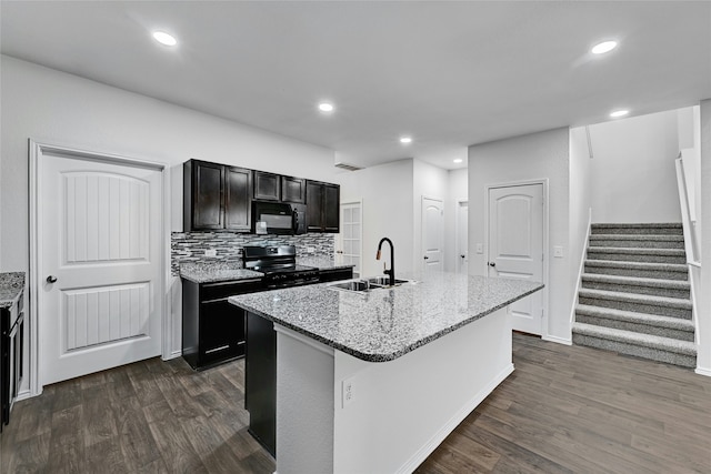 kitchen featuring light stone countertops, black appliances, a kitchen island with sink, backsplash, and sink