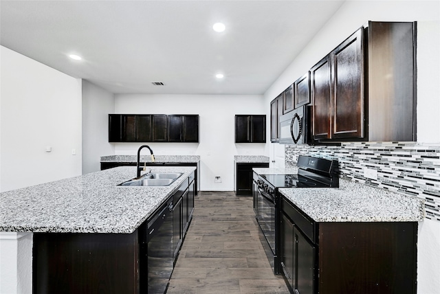 kitchen featuring a center island with sink, black appliances, dark hardwood / wood-style flooring, sink, and backsplash