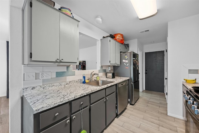 kitchen with sink, light hardwood / wood-style flooring, gray cabinets, tasteful backsplash, and stainless steel appliances