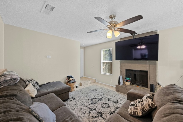 tiled living room featuring a fireplace, a textured ceiling, and ceiling fan