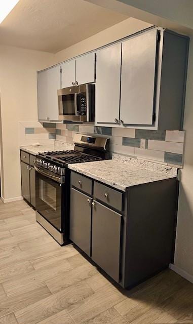 kitchen with stainless steel appliances, light hardwood / wood-style flooring, tasteful backsplash, and gray cabinetry