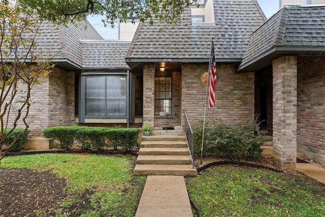 view of exterior entry with mansard roof, brick siding, and a shingled roof