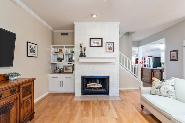 living area with stairway, visible vents, light wood-style flooring, ornamental molding, and a brick fireplace