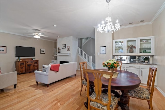 dining area featuring crown molding, a fireplace, light hardwood / wood-style floors, and ceiling fan with notable chandelier