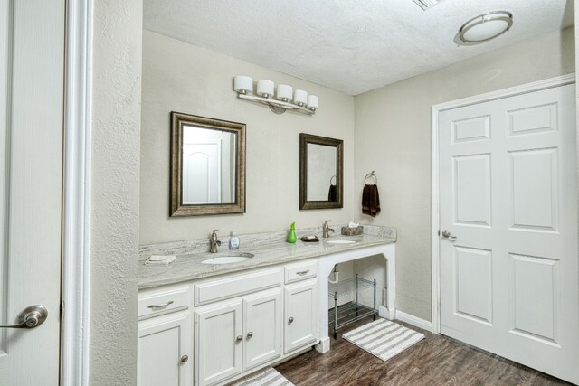 bathroom with double vanity, a textured ceiling, wood finished floors, and a sink