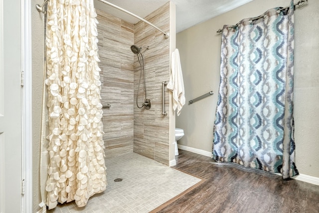 full bathroom with toilet, wood finished floors, baseboards, and tiled shower