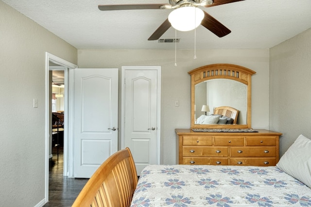 bedroom featuring visible vents, dark wood-style floors, a ceiling fan, and a textured wall