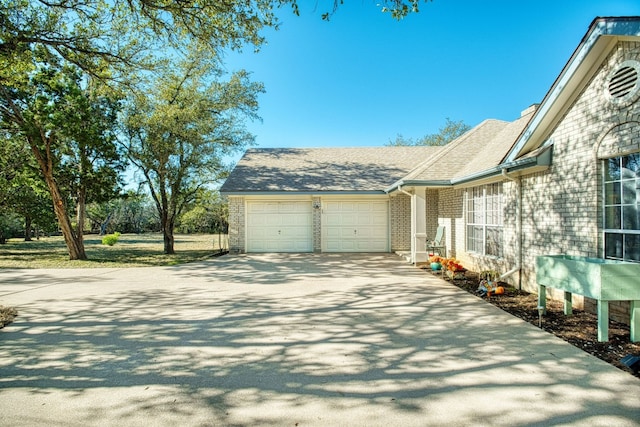 view of side of property featuring brick siding, an attached garage, a shingled roof, and driveway