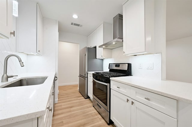 kitchen featuring appliances with stainless steel finishes, light wood-type flooring, wall chimney range hood, sink, and white cabinets