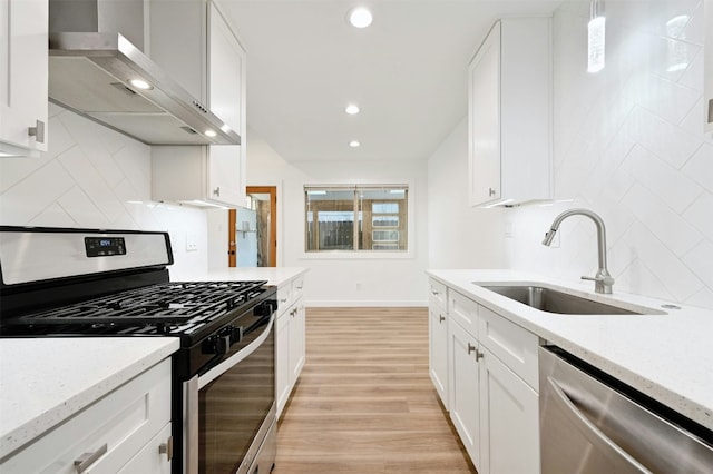 kitchen featuring white cabinetry, wall chimney range hood, sink, and appliances with stainless steel finishes