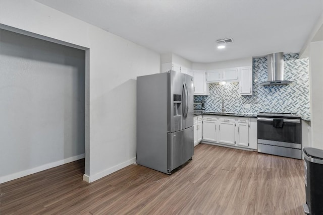 kitchen featuring hardwood / wood-style floors, white cabinetry, wall chimney range hood, and stainless steel appliances