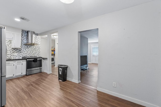 kitchen featuring white cabinets, wall chimney exhaust hood, stainless steel appliances, and light hardwood / wood-style flooring