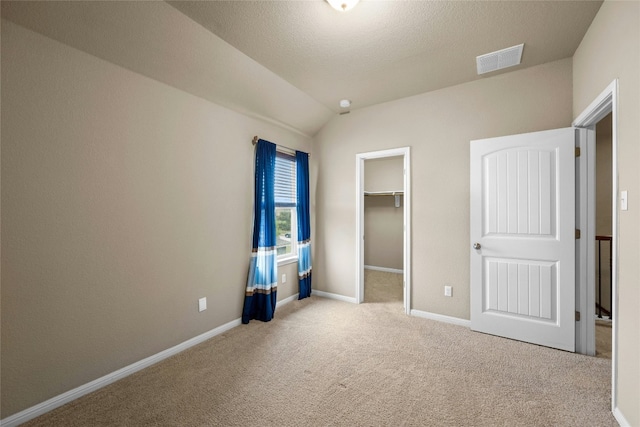 unfurnished bedroom with lofted ceiling, a walk in closet, light carpet, and a closet