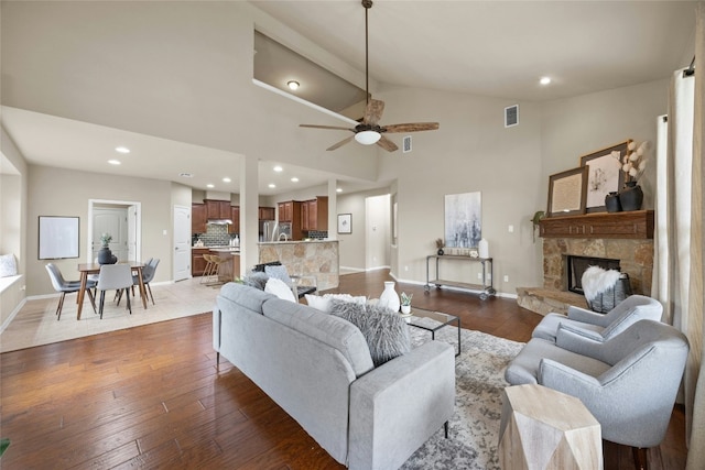 living room with wood-type flooring, high vaulted ceiling, a stone fireplace, and ceiling fan