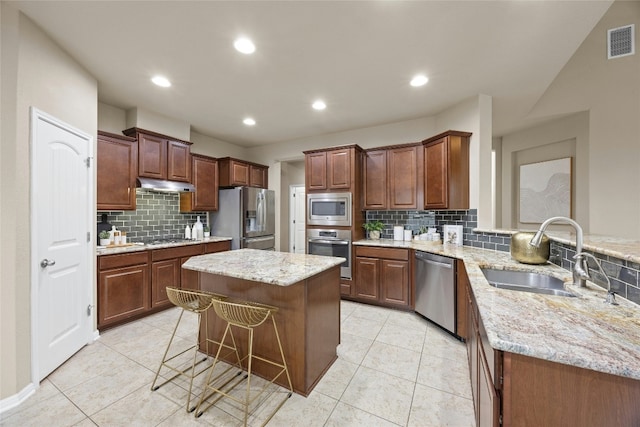 kitchen with a kitchen bar, tasteful backsplash, stainless steel appliances, sink, and a kitchen island