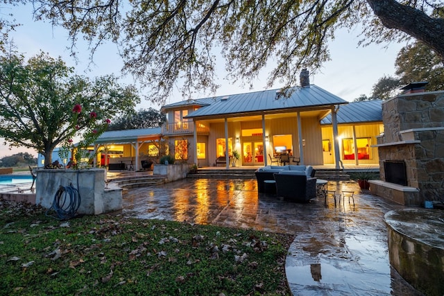 back house at dusk featuring an outdoor living space with a fireplace, a patio area, and a bar