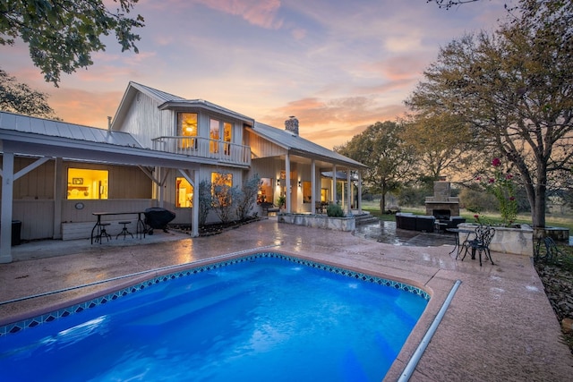 pool at dusk featuring a patio area and an outdoor stone fireplace