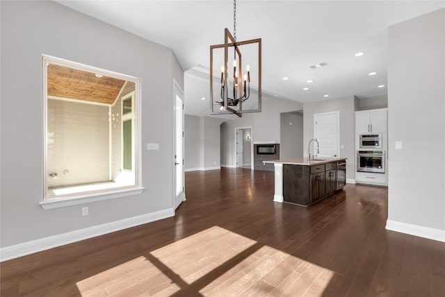 kitchen with a kitchen island with sink, dark wood-type flooring, sink, decorative light fixtures, and a notable chandelier