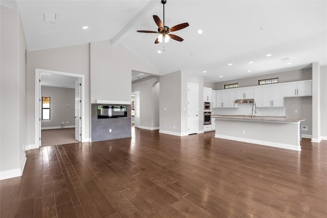 unfurnished living room featuring dark wood-type flooring, high vaulted ceiling, sink, ceiling fan, and beam ceiling