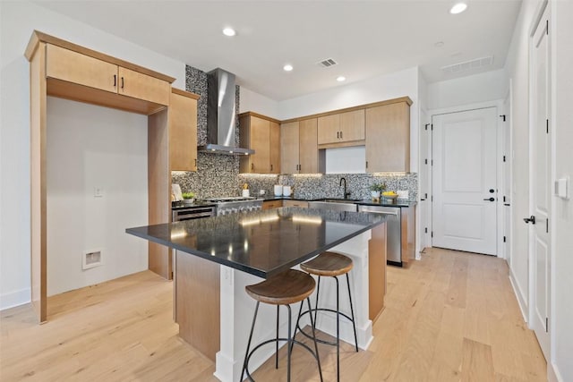 kitchen with wall chimney range hood, light hardwood / wood-style flooring, decorative backsplash, a kitchen island, and stainless steel appliances