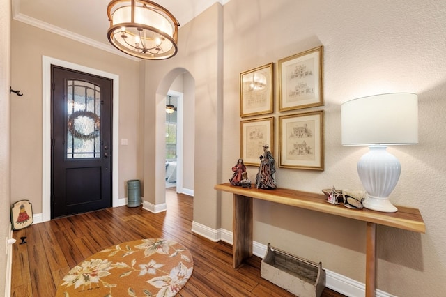 foyer entrance featuring an inviting chandelier, crown molding, and dark wood-type flooring