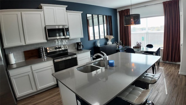 kitchen featuring pendant lighting, a kitchen island with sink, white cabinets, sink, and appliances with stainless steel finishes