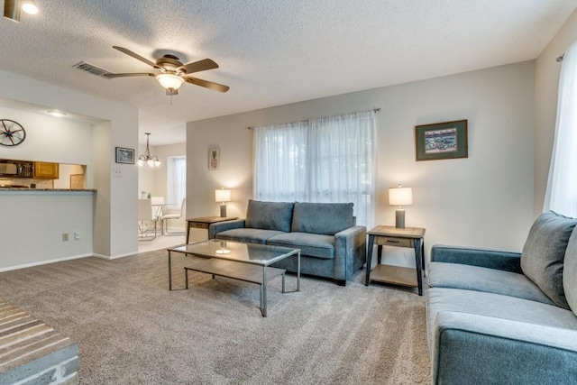 living room featuring carpet flooring, ceiling fan with notable chandelier, and a textured ceiling