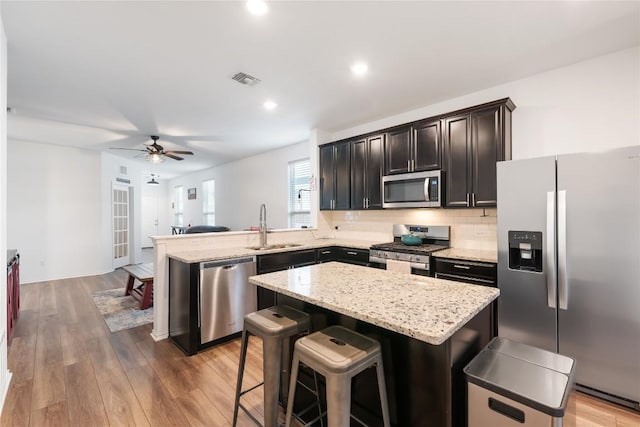 kitchen with sink, a center island, stainless steel appliances, kitchen peninsula, and hardwood / wood-style flooring